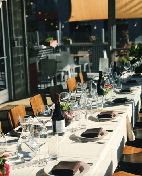 A beautifully set dining table with glassware and wine bottles, ready for a meal in a bright, modern restaurant.