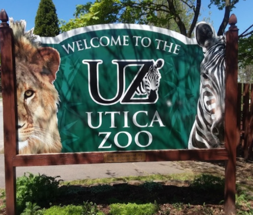 Sign welcoming visitors to Utica Zoo, featuring a lion and a zebra on a green background.