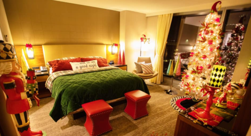 Cozy bedroom decorated for the holidays, featuring a Christmas tree, festive decor, and a green bedspread.