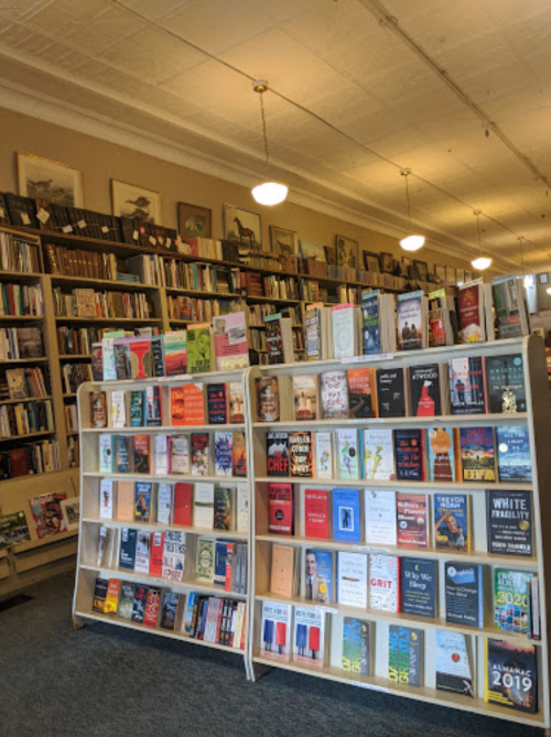 A cozy bookstore with shelves filled with various books, featuring a display of titles in the foreground.
