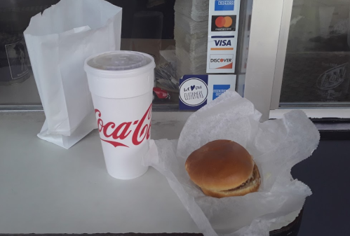 A Coca-Cola cup, a sandwich wrapped in paper, and a takeout bag on a table.
