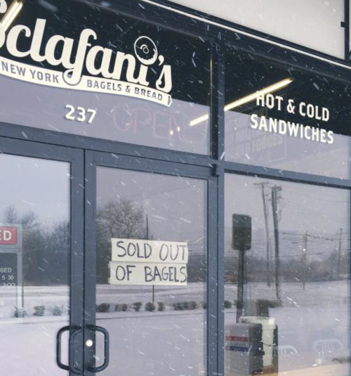 A storefront with a sign reading "Sold Out of Bagels" in snowy weather, featuring the name "Sclafani's" above.