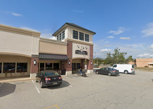 A storefront with a tower, surrounded by parked cars and a clear blue sky.