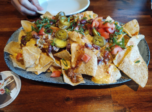 A platter of nachos topped with cheese, jalapeños, tomatoes, green onions, and beans on a wooden table.