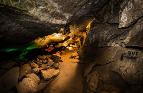 A dimly lit cave interior with rocky walls, scattered boulders, and colorful lights illuminating the space.