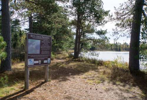 A trail leading to a lake, with a sign for Bete Grise Preserve surrounded by trees and autumn foliage.