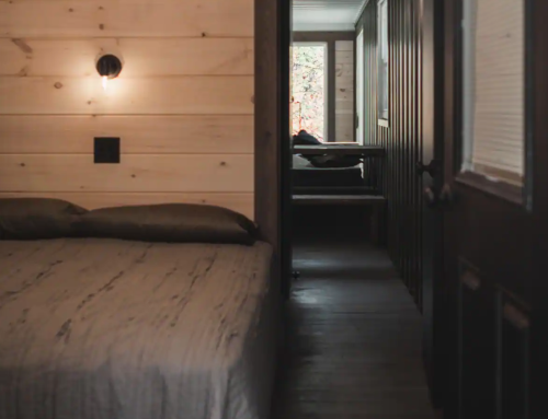 Cozy interior of a cabin with a bed in the foreground and a doorway leading to another room in the background.