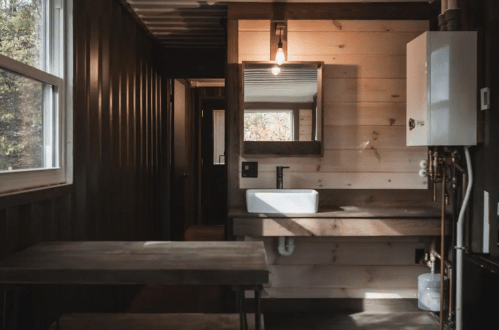 A modern, rustic bathroom with a wooden sink, mirror, and a table, featuring natural light from windows.