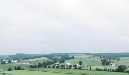 A scenic view of rolling green fields and farms under a cloudy sky.