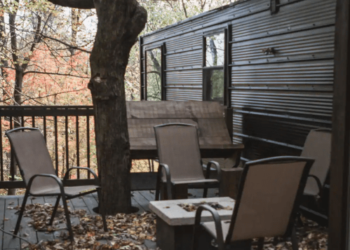 A cozy outdoor deck with four chairs, a table, and a tree, surrounded by autumn foliage.