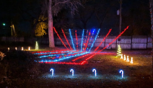 Colorful holiday lights create a festive display in a yard, featuring trees and candy canes against a dark night sky.