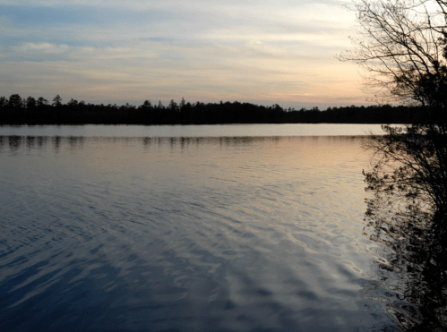 A tranquil lake at sunset, with calm waters reflecting the sky and trees along the shore.