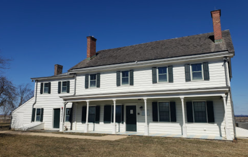 A large white two-story house with green shutters and a porch, set against a clear blue sky.