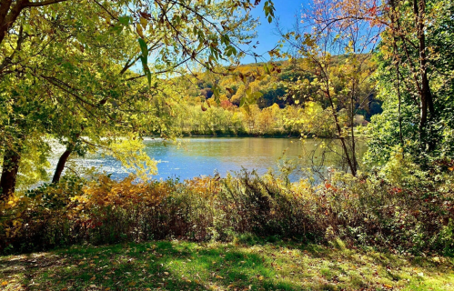 A serene river scene surrounded by vibrant autumn foliage and trees under a clear blue sky.