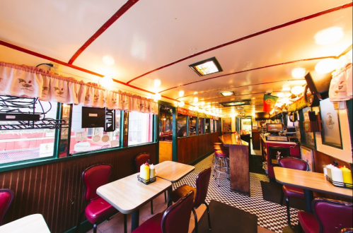 Interior of a retro diner with checkered floor, red booths, and warm lighting, creating a cozy atmosphere.