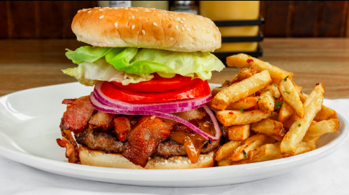 A juicy burger with bacon, lettuce, tomato, and onion, served with a side of crispy fries on a white plate.