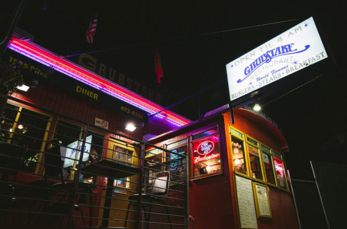 A brightly lit diner at night with neon signs, featuring a sign that says "Open 'til 4 AM" and a menu board.