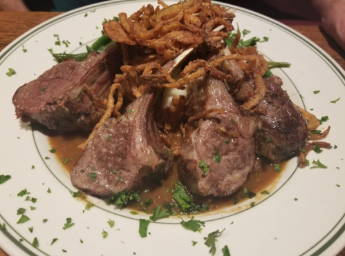 A plate of lamb chops topped with crispy fried onions, garnished with parsley and served in a savory sauce.