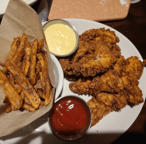A plate of crispy fried chicken strips, served with fries, ketchup, and a creamy dipping sauce.
