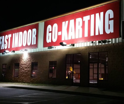 A brightly lit building at night with large red signs reading "EAST INDOOR GO-KARTING." Windows are visible.