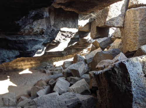 A rocky cave interior with scattered boulders and shafts of light illuminating the space.
