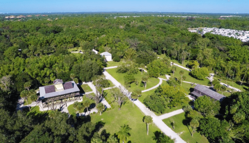 Aerial view of a lush green landscape with pathways and buildings surrounded by trees.