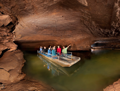 A group of people on a boat exploring a cave with rock formations and green water.