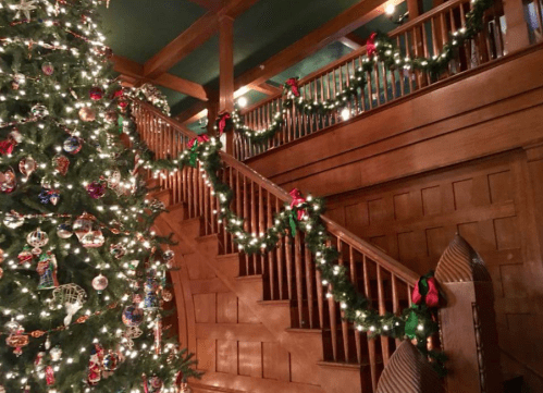 A beautifully decorated staircase with garlands and a large Christmas tree adorned with ornaments and lights.