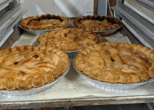 Five freshly baked pies cooling on a tray, featuring golden-brown crusts and varying fillings.