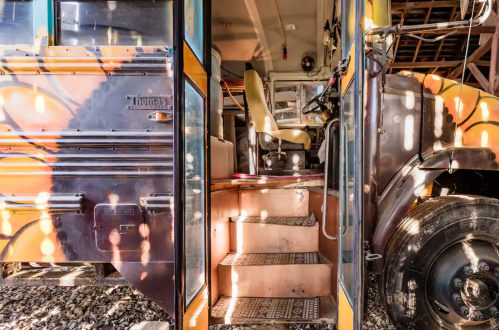 Interior view of a colorful bus with steps leading up to the driver's seat, illuminated by soft light.