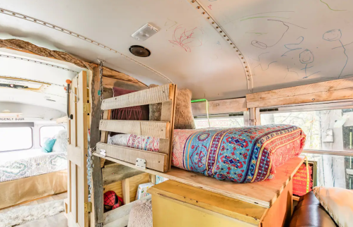 Interior of a converted bus featuring a cozy sleeping area with colorful bedding and wooden accents.