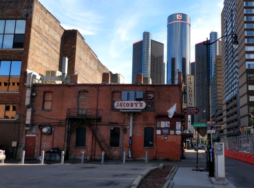 A brick building with a sign reading "Jacoby's" in an urban setting, with modern skyscrapers in the background.