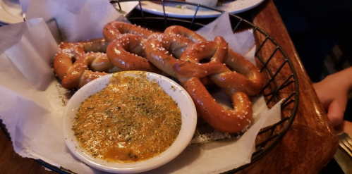 A basket of soft pretzels with coarse salt, served with a small bowl of mustard dip.
