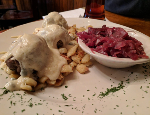 A plate of meatballs covered in creamy sauce on a bed of pasta, served with a side of pickled red cabbage.