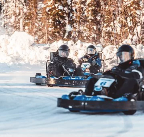 Three go-karts racing on a snowy track, surrounded by trees and winter scenery.