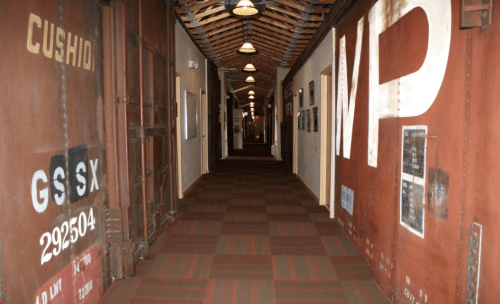 A long hallway with industrial-style walls, featuring metal doors and overhead lights, creating a vintage atmosphere.