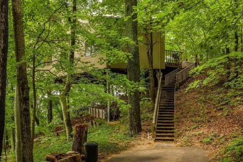 A modern treehouse nestled among lush green trees, with wooden stairs leading up to it.