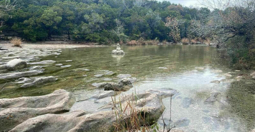 A serene landscape featuring a clear, shallow river surrounded by rocky banks and lush greenery.
