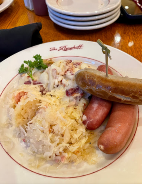 A plate of sauerkraut with two types of sausages, garnished with a parsley sprig, served at a restaurant.