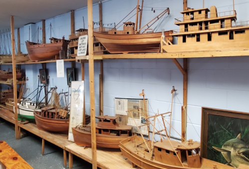 A display of wooden ship models on shelves in a museum, showcasing various boat designs and sizes.