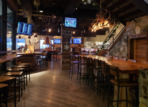 A cozy restaurant interior with wooden bar seating, stone accents, and multiple TVs displaying sports.