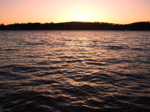 Sunset over a calm lake, with gentle waves reflecting warm hues of orange and pink in the sky.