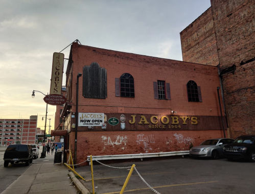 Exterior of Jacoby's restaurant, a red brick building with a sign, located in an urban area at dusk.