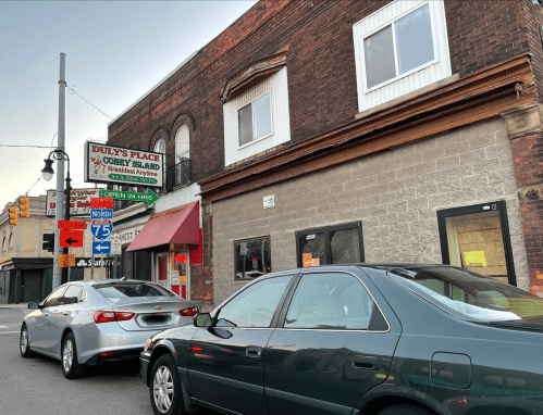A street view of Duly's Place, a 24-hour diner, with parked cars and a sign for nearby highways.