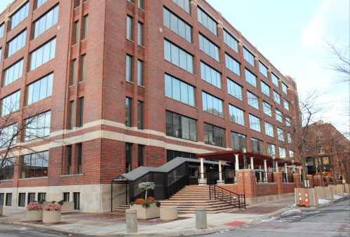 A modern brick building with large windows and a staircase leading to the entrance, set in an urban environment.