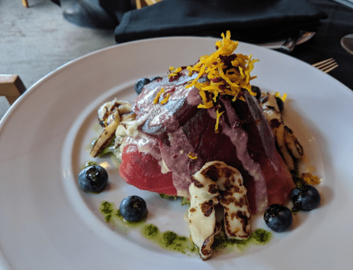 A colorful dish featuring sliced meat, cheese, blueberries, and garnished with orange zest on a white plate.