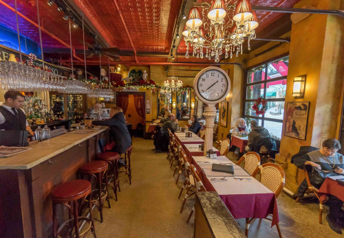 A cozy restaurant interior with a bar, tables set for dining, and patrons enjoying their meals in a warm atmosphere.