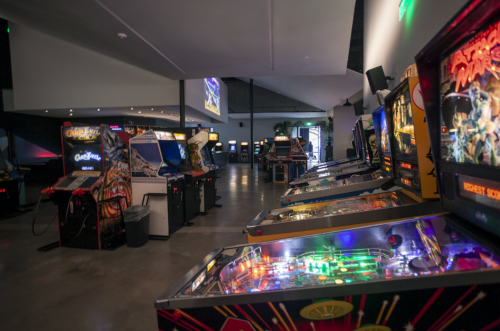 A spacious arcade with rows of colorful pinball machines and classic arcade games under soft lighting.