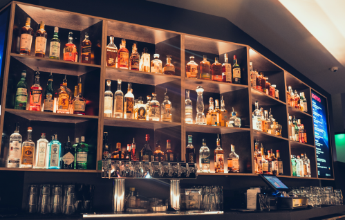 A well-stocked bar with shelves of various liquor bottles and a bar counter with glasses and a menu display.
