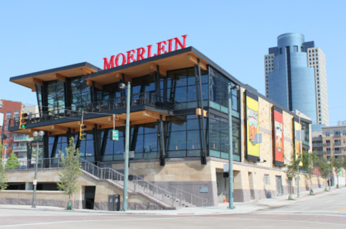 Modern building with large glass windows and a red "Moerlein" sign, located in an urban area with skyscrapers in the background.